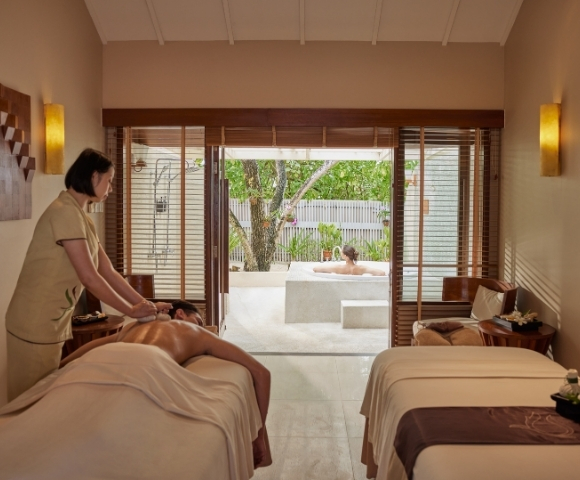 A serene spa room with a therapist giving a massage to a client, while another person enjoys a relaxing soak in a private outdoor tub.