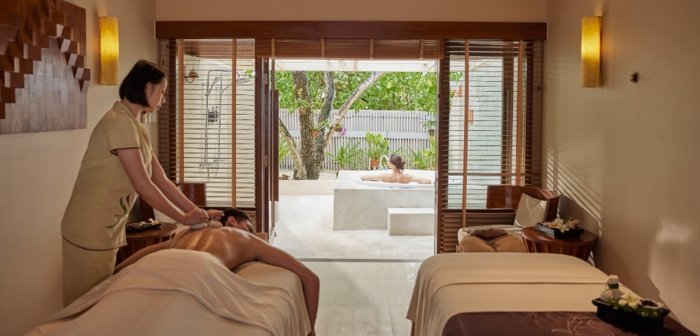 A serene spa room with a therapist giving a massage to a client, while another person enjoys a relaxing soak in a private outdoor tub.
