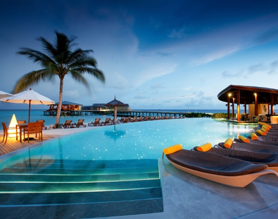 Elegant resort pool at dusk, with lounge chairs, palm trees, and ocean views, creating a tranquil vacation atmosphere.