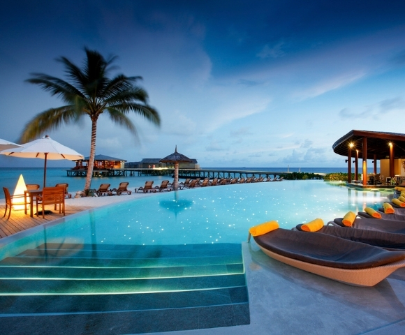 Elegant resort pool at dusk, with lounge chairs, palm trees, and ocean views, creating a tranquil vacation atmosphere.