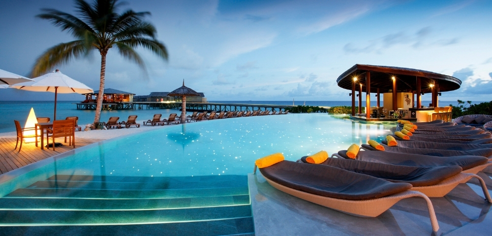 Elegant resort pool at dusk, with lounge chairs, palm trees, and ocean views, creating a tranquil vacation atmosphere.