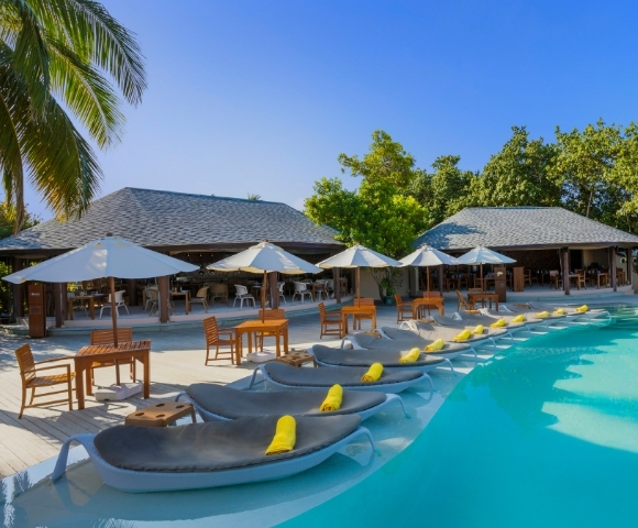 Serene poolside scene with loungers and umbrellas, surrounded by tropical foliage and a modern restaurant in the background.
