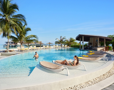 A serene poolside scene featuring a woman relaxing on a lounge chair and a man swimming, surrounded by palm trees and sunny skies.