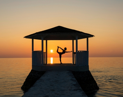Silhouette of a person practicing yoga in a pavilion by the sea at sunset, creating a serene and tranquil atmosphere.