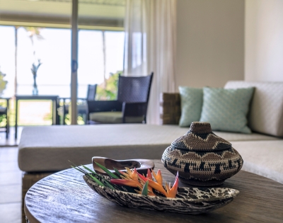 A cozy living area featuring a stylish woven basket and vibrant flowers on a wooden table, with a view of the outdoors beyond.