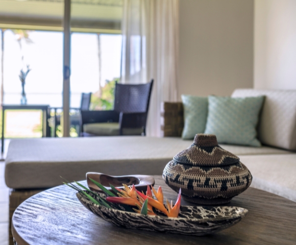 A cozy living area featuring a stylish woven basket and vibrant flowers on a wooden table, with a view of the outdoors beyond.