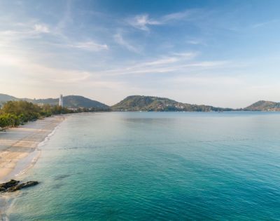 A serene beach view with gentle waves, soft sand, and distant hills under a clear blue sky, evoking tranquility and natural beauty.