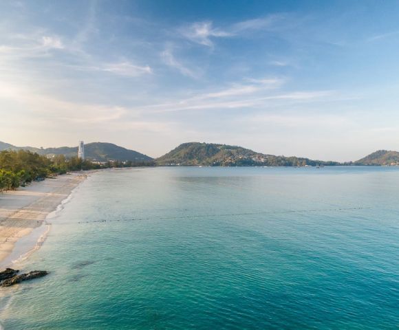 A serene beach view with gentle waves, soft sand, and distant hills under a clear blue sky, evoking tranquility and natural beauty.