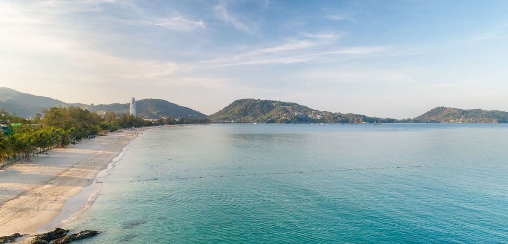 A serene beach view with gentle waves, soft sand, and distant hills under a clear blue sky, evoking tranquility and natural beauty.