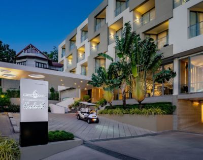 Modern hotel entrance featuring tropical plants, a golf cart, and stylish architecture under an evening sky.