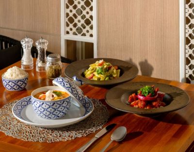 An elegant dining table featuring three Asian dishes: curry, fried rice, and a seafood stew, alongside condiments and rice in decorative bowls.