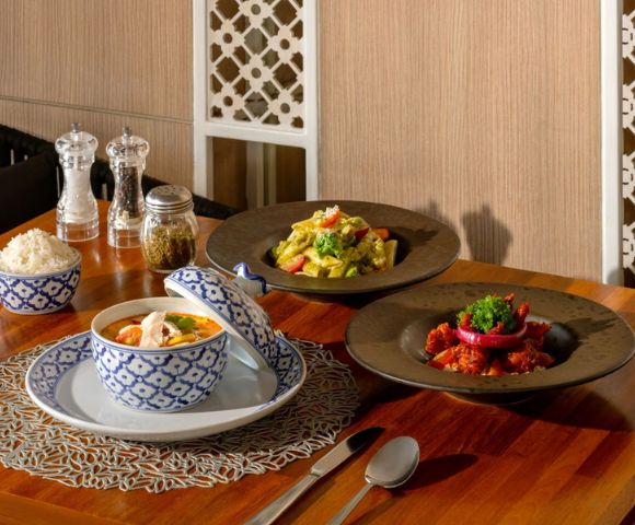 An elegant dining table featuring three Asian dishes: curry, fried rice, and a seafood stew, alongside condiments and rice in decorative bowls.