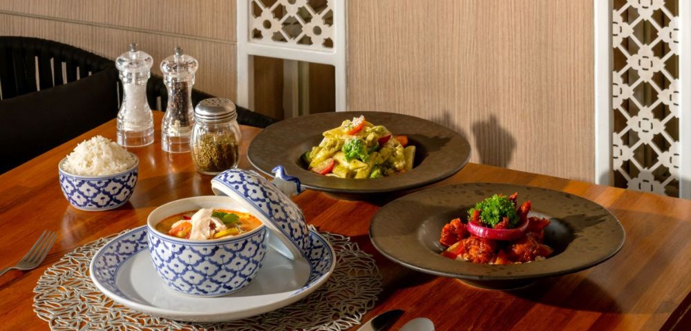 An elegant dining table featuring three Asian dishes: curry, fried rice, and a seafood stew, alongside condiments and rice in decorative bowls.