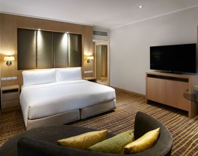 Modern hotel room featuring a queen bed, stylish seating area, flat-screen TV, and warm lighting.