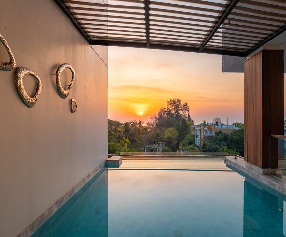 Sunset view from a luxurious poolside, with modern artwork on the wall and a serene landscape beyond.