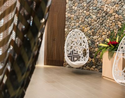 A cozy interior featuring a hanging white chair and a decorative stone wall, alongside a tropical plant arrangement.