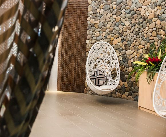 A cozy interior featuring a hanging white chair and a decorative stone wall, alongside a tropical plant arrangement.