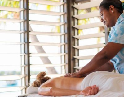 A therapist gives a relaxing massage to a client in a bright room with large windows and palm trees visible outside.