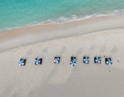 Aerial view of a sandy beach with striped blue and white umbrellas arranged in neat rows along the shoreline by turquoise waters.