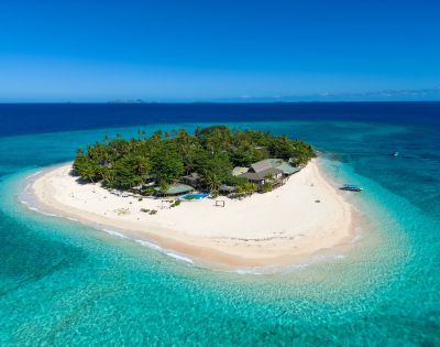 Aerial view of a tropical island with white sand, lush palm trees, and clear blue waters under a bright sky. Ideal for paradise getaways.