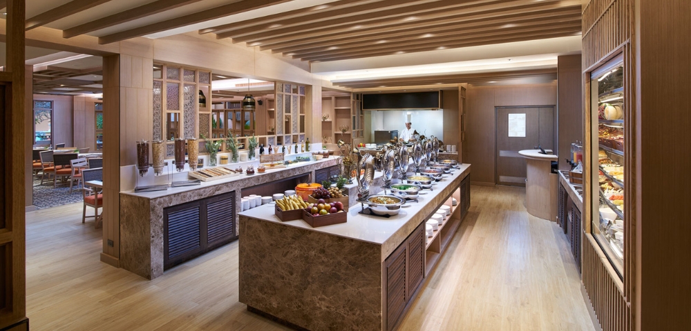 A elegant dining area featuring a buffet with various fruits, salads, and dishes, surrounded by wooden decor and warm lighting.