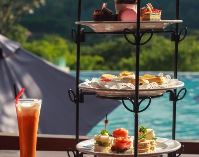 A tiered stand displays an assortment of pastries and sandwiches, with a refreshing drink beside it, set against a scenic background.