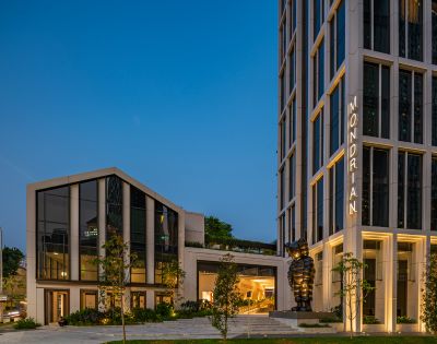Modern Mondrian hotel exterior at dusk, featuring sleek architecture, greenery, and a prominent black sculpture.