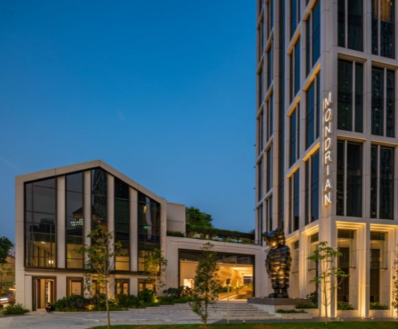 Modern Mondrian hotel exterior at dusk, featuring sleek architecture, greenery, and a prominent black sculpture.