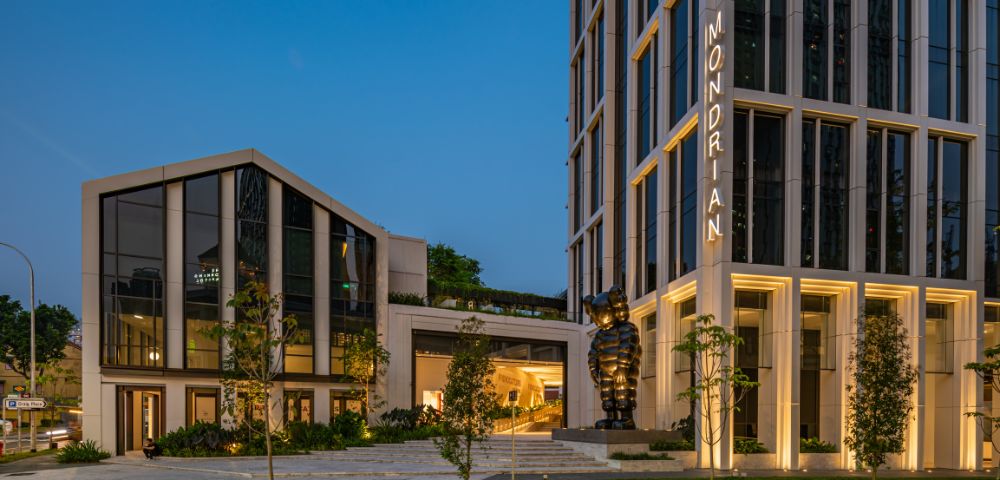 Modern Mondrian hotel exterior at dusk, featuring sleek architecture, greenery, and a prominent black sculpture.