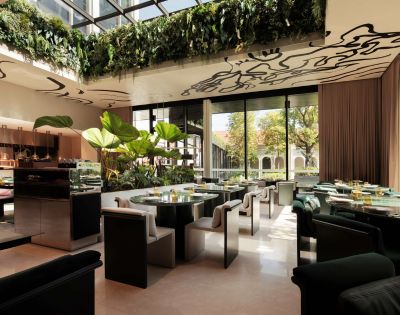 A chic restaurant interior featuring green plants, elegant seating, and large windows for natural light, enhancing a sophisticated dining atmosphere.