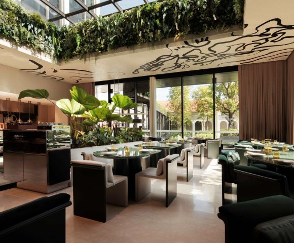 A chic restaurant interior featuring green plants, elegant seating, and large windows for natural light, enhancing a sophisticated dining atmosphere.