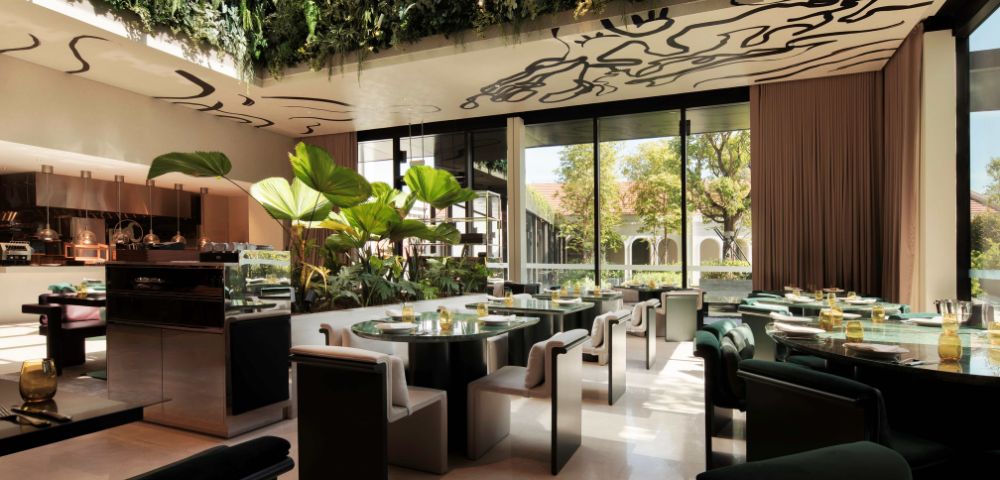A chic restaurant interior featuring green plants, elegant seating, and large windows for natural light, enhancing a sophisticated dining atmosphere.