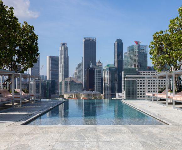 Rooftop infinity pool overlooking a vibrant city skyline, with lounge chairs and greenery adding to the luxurious ambiance.