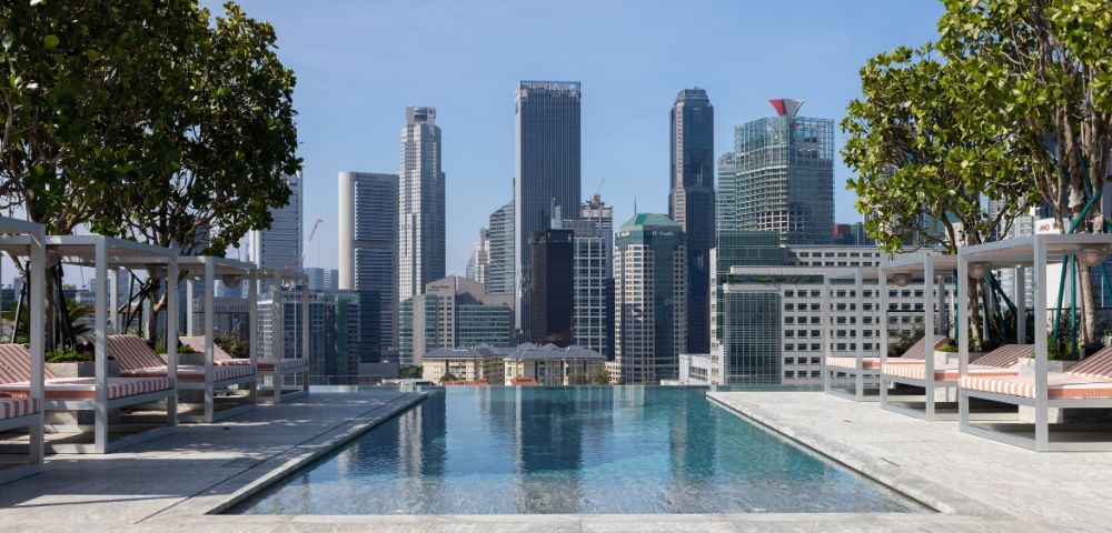Rooftop infinity pool overlooking a vibrant city skyline, with lounge chairs and greenery adding to the luxurious ambiance.