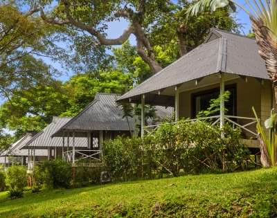 Three charming cottages with metal roofs nestled among lush greenery and trees under a clear blue sky.
