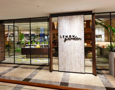 Entrance of Lemon Garden restaurant, featuring a stylish sign and glass walls, with a view of lush greenery inside.