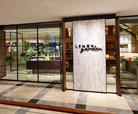 Entrance of Lemon Garden restaurant, featuring a stylish sign and glass walls, with a view of lush greenery inside.