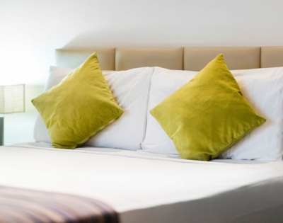 A neatly made bed with two vibrant green pillows against a light beige headboard and a soft striped blanket at the foot.