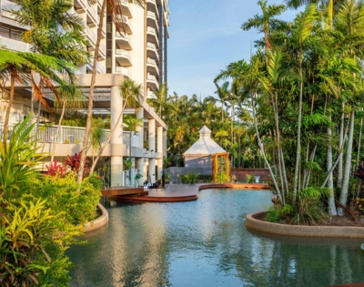 Lush tropical landscape featuring a serene swimming pool surrounded by greenery and a modern building with balconies.