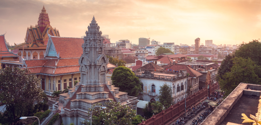 Panoramic view of Phnom Penh at sunset, featuring traditional Khmer architecture and bustling cityscape in warm hues.
