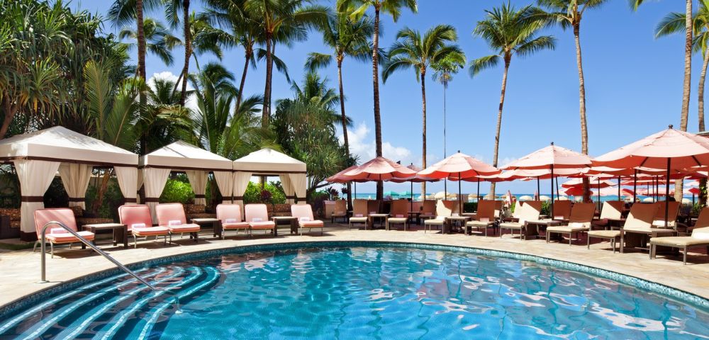 A luxurious pool surrounded by palm trees, cabanas, and lounge chairs under colorful umbrellas, offering a tropical resort vibe.