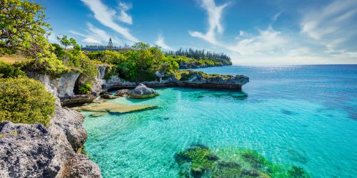 A serene coastal scene featuring crystal clear turquoise waters, lush greenery, and rocky cliffs under a bright blue sky.