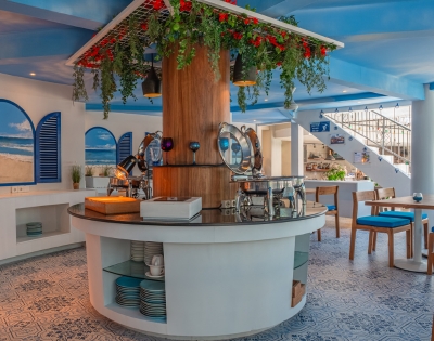 Stylish dining area with a circular buffet, blue decor, lush greenery, and beach-themed wall art, creating a vibrant and inviting atmosphere.
