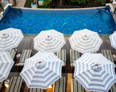 Aerial view of a vibrant blue swimming pool surrounded by striped umbrellas and lounge chairs, inviting relaxation.