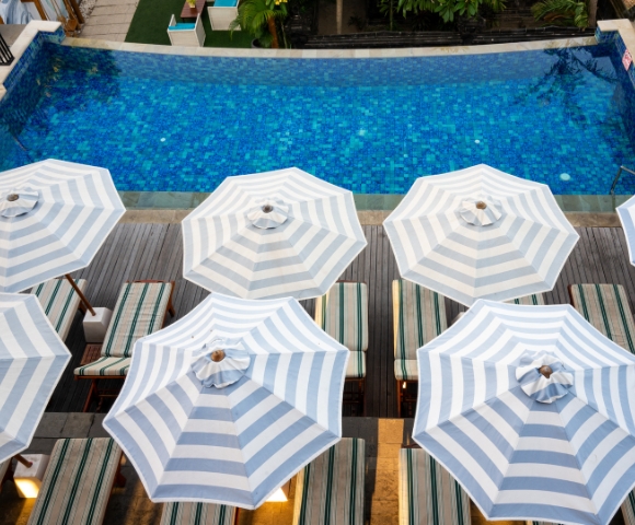 Aerial view of a vibrant blue swimming pool surrounded by striped umbrellas and lounge chairs, inviting relaxation.