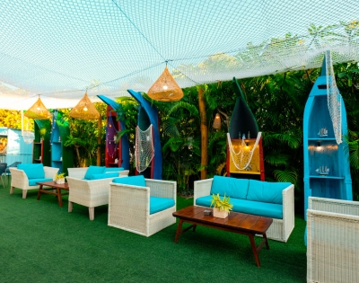 Cozy outdoor lounge with white wicker seating, vibrant blue cushions, surfboard decor, and greenery under a netted canopy.