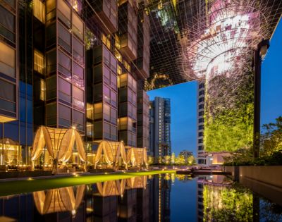 A luxurious hotel exterior at night, featuring modern architecture, illuminated terraces, and reflections on a tranquil pool.
