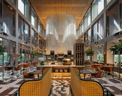 Modern restaurant interior with high ceilings, large windows, stylish seating, and a striking feature wall adorned with shimmering tiles.