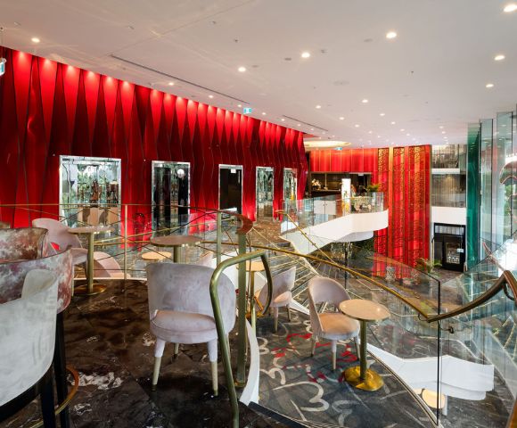 Elegant restaurant interior featuring red walls, plush seating, and modern decor, with a stylish staircase and large windows.