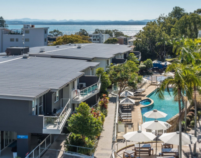 Aerial view of modern apartments with a swimming pool and sun loungers, overlooking a scenic waterfront landscape.